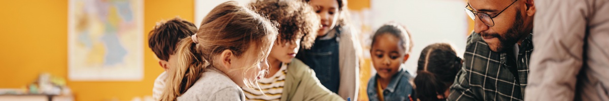 School-aged children gathered around a teacher in a classroom setting.