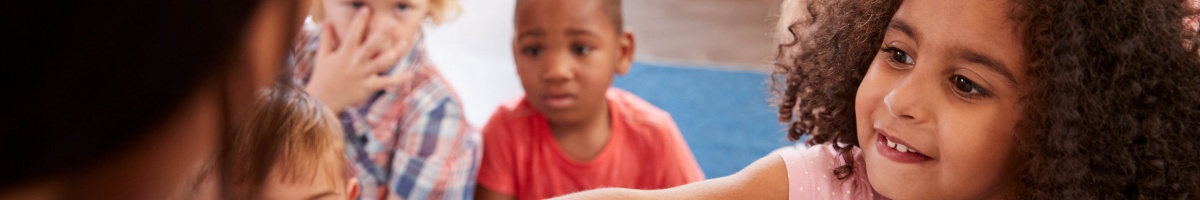 A girl points to a large chart during full class reading instruction.