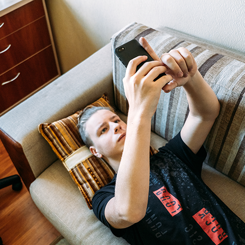 young male laying on couch looking up and mobile phone held in both hands