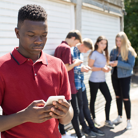 Young man viewing his phone. Friends in the background blurred. 