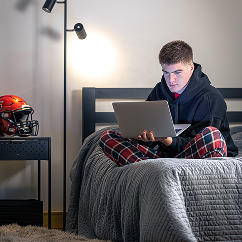 Teenage bot sitting on his bed with a laptop computer in his lap